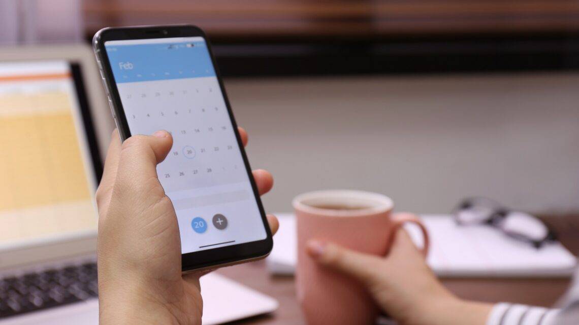 Frau hält Smartphone mit geöffnetem Kalender in der Hand
